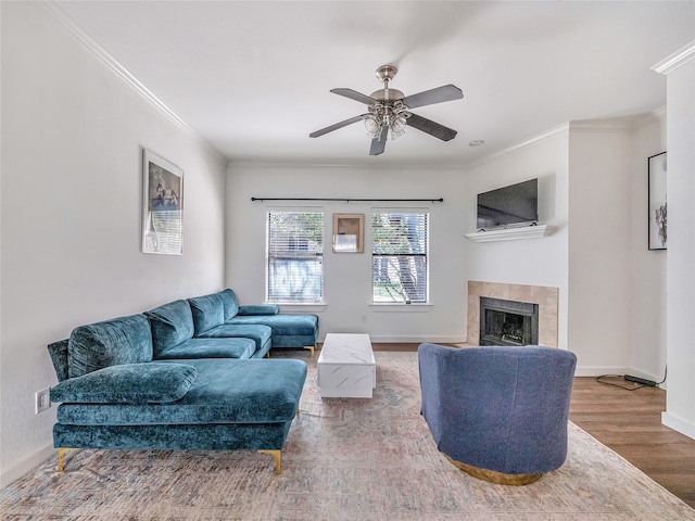 living room with ceiling fan, wood-type flooring, crown molding, and a tiled fireplace