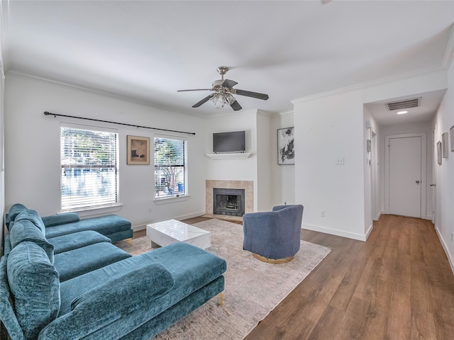 living room with a tile fireplace, ceiling fan, hardwood / wood-style floors, and ornamental molding