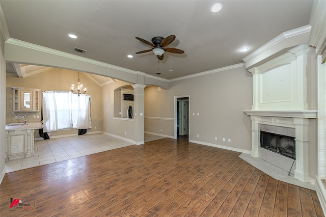 unfurnished living room with ceiling fan with notable chandelier, crown molding, light wood-type flooring, a tile fireplace, and lofted ceiling