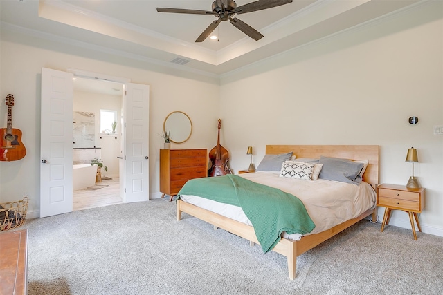 carpeted bedroom with ornamental molding, connected bathroom, a tray ceiling, and ceiling fan