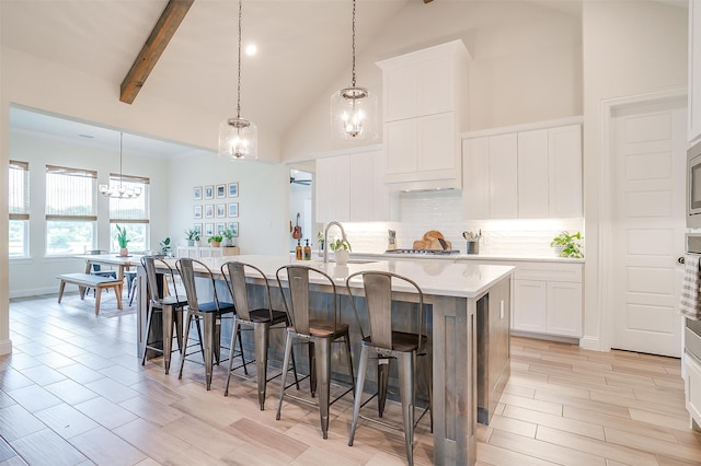 kitchen featuring high vaulted ceiling, white cabinets, beam ceiling, and a center island with sink