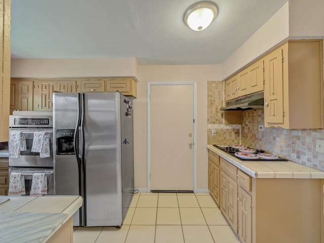 kitchen with light tile patterned floors, backsplash, stainless steel appliances, and light brown cabinetry