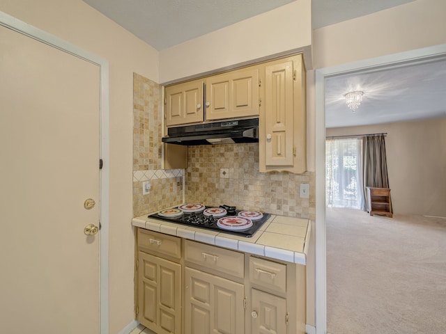 kitchen with black gas stovetop, tile countertops, light carpet, light brown cabinetry, and backsplash