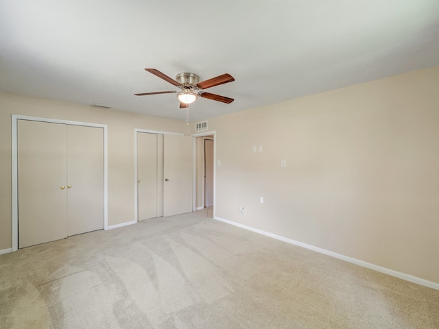 unfurnished bedroom with ceiling fan, two closets, and light carpet