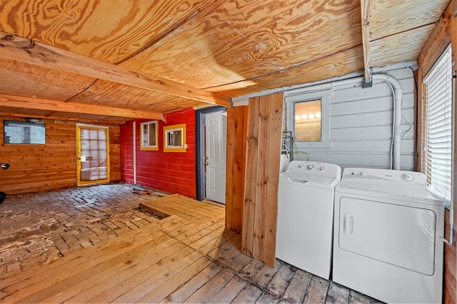 clothes washing area with separate washer and dryer, a wealth of natural light, hardwood / wood-style floors, and wooden walls