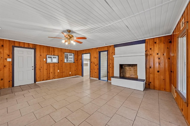 unfurnished living room with a fireplace with raised hearth, ceiling fan, light tile patterned flooring, and wooden walls