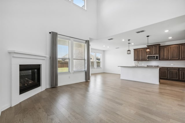 unfurnished living room featuring light wood-type flooring, sink, and a high ceiling