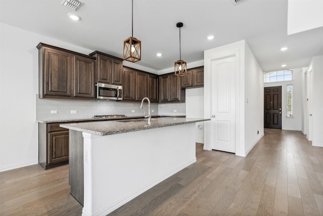 kitchen with light hardwood / wood-style flooring, tasteful backsplash, a kitchen island with sink, sink, and dark brown cabinets