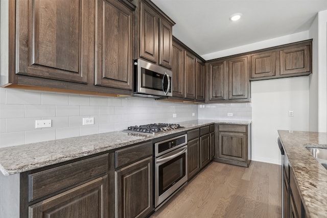 kitchen with light hardwood / wood-style flooring, backsplash, light stone counters, stainless steel appliances, and dark brown cabinets