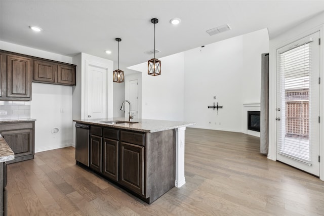 kitchen featuring dark brown cabinetry, wood-type flooring, light stone countertops, a kitchen island with sink, and dishwasher