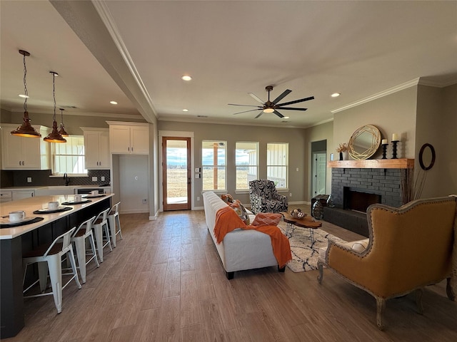 living room featuring ceiling fan, ornamental molding, a brick fireplace, and light wood-type flooring