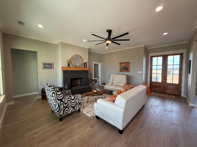 living room with wood-type flooring, ornamental molding, ceiling fan, a brick fireplace, and french doors