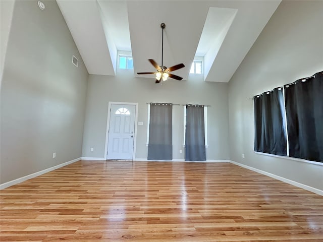 unfurnished living room with light wood finished floors, baseboards, visible vents, a ceiling fan, and high vaulted ceiling