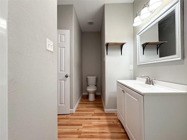 half bathroom with baseboards, visible vents, toilet, wood finished floors, and vanity