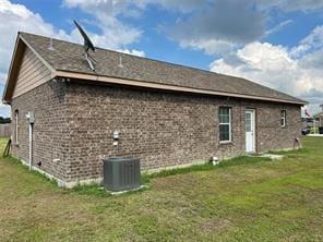 rear view of house with central AC, brick siding, and a lawn