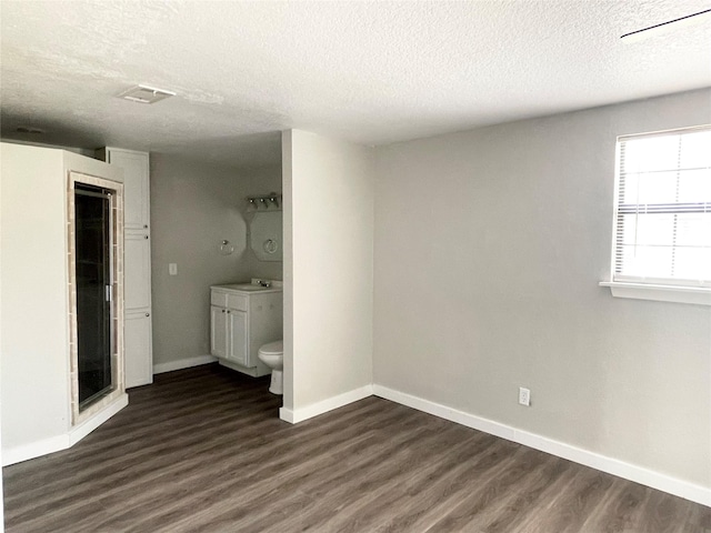 unfurnished bedroom featuring dark hardwood / wood-style floors, sink, a textured ceiling, and ensuite bath