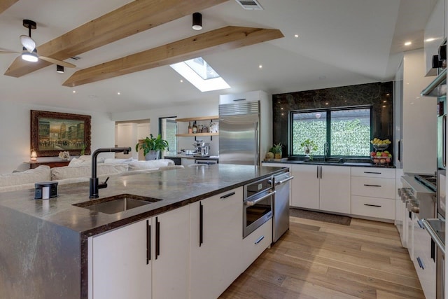 kitchen featuring sink, dark stone countertops, white cabinets, stainless steel appliances, and light wood-type flooring