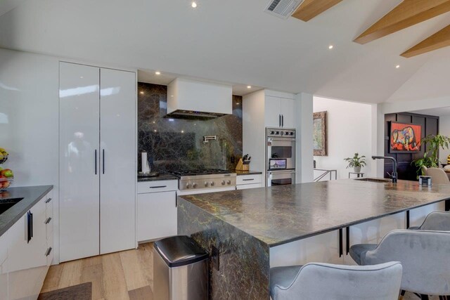 kitchen featuring premium range hood, lofted ceiling, sink, white cabinets, and decorative backsplash