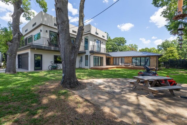 rear view of property with a balcony, a garage, and a lawn