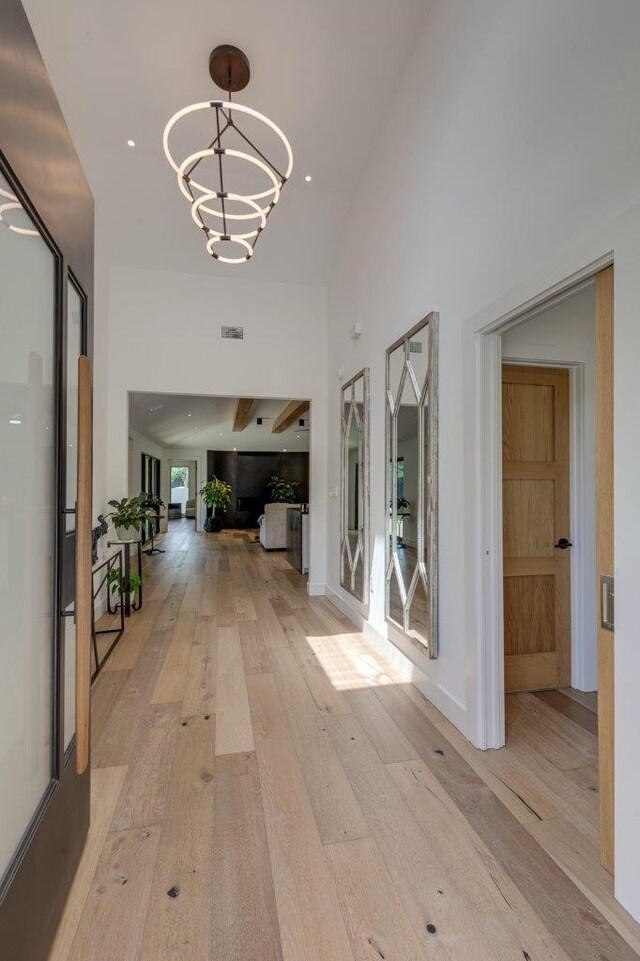 hallway featuring a towering ceiling, a chandelier, and light hardwood / wood-style flooring