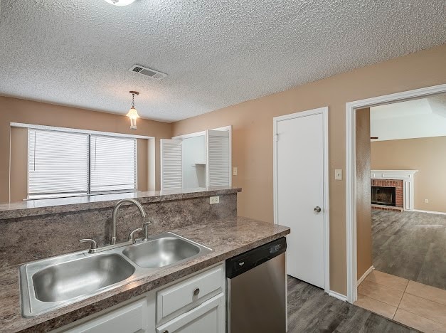 kitchen featuring white cabinets, stainless steel dishwasher, a brick fireplace, hardwood / wood-style floors, and sink