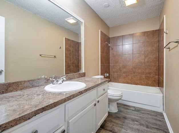 full bathroom with vanity, hardwood / wood-style flooring, tiled shower / bath, toilet, and a textured ceiling