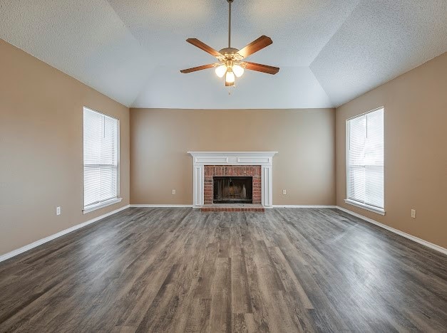 unfurnished living room featuring plenty of natural light, a brick fireplace, wood-type flooring, and lofted ceiling