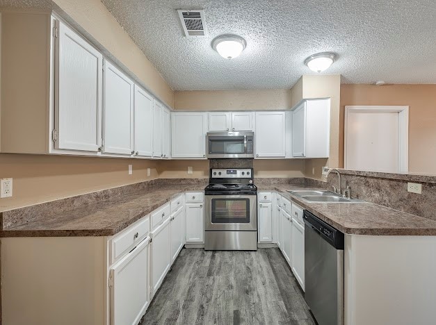 kitchen featuring appliances with stainless steel finishes, light hardwood / wood-style flooring, white cabinets, sink, and a textured ceiling