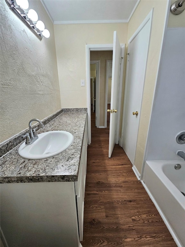 bathroom with vanity, a bathtub, hardwood / wood-style flooring, and crown molding