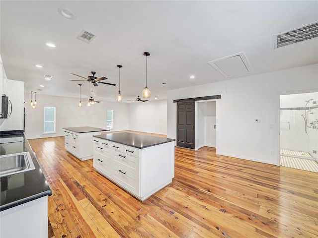 kitchen with white cabinetry, ceiling fan, a barn door, a center island, and light hardwood / wood-style floors