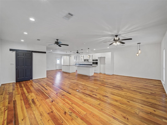 unfurnished living room with sink, light wood-type flooring, and ceiling fan