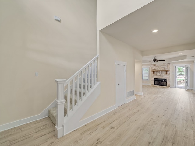 staircase with a stone fireplace, ceiling fan, and light hardwood / wood-style floors