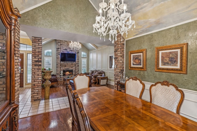 dining space with hardwood / wood-style floors, decorative columns, a notable chandelier, a brick fireplace, and vaulted ceiling