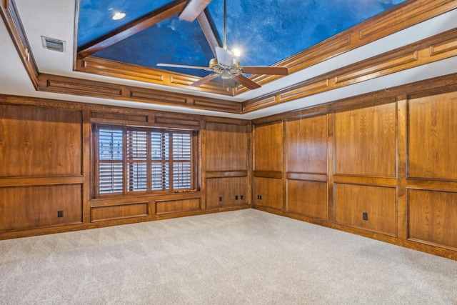 carpeted empty room with a raised ceiling, crown molding, and wooden walls