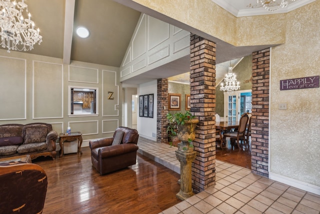 living room with ornate columns, a towering ceiling, a chandelier, hardwood / wood-style flooring, and crown molding