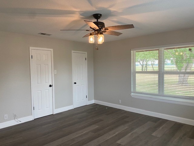 empty room featuring visible vents, baseboards, and dark wood finished floors