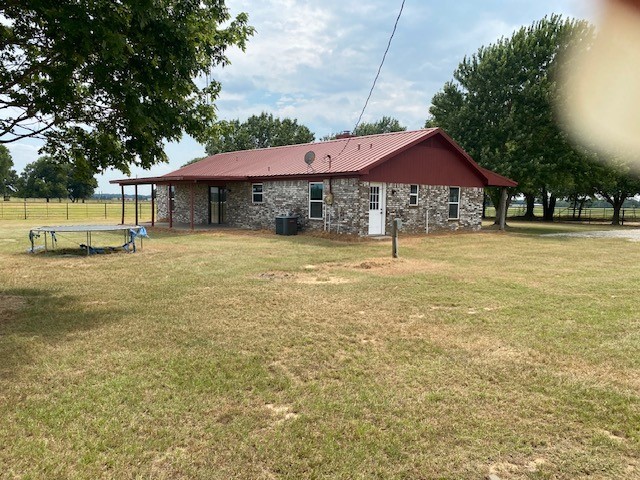 rear view of property with stone siding, metal roof, a trampoline, fence, and a yard