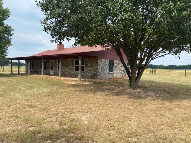 back of house with brick siding, a yard, a chimney, fence, and a carport