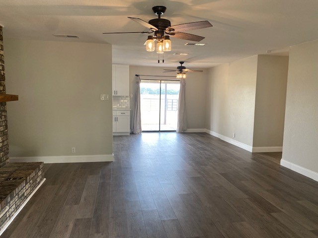 unfurnished living room with visible vents, baseboards, a ceiling fan, dark wood-type flooring, and a fireplace