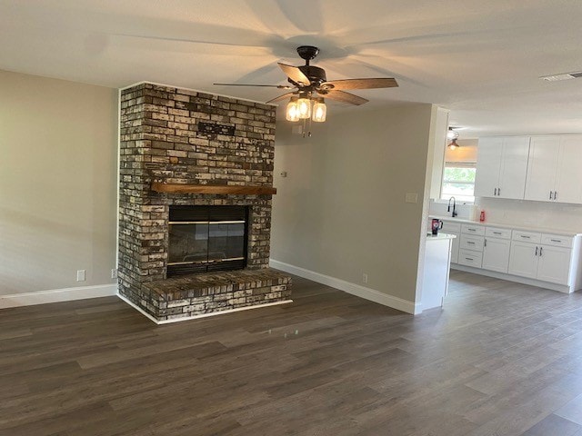 unfurnished living room with brick wall, a fireplace, dark hardwood / wood-style floors, and ceiling fan