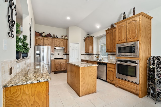 kitchen featuring light tile patterned floors, a center island, light stone countertops, appliances with stainless steel finishes, and decorative backsplash