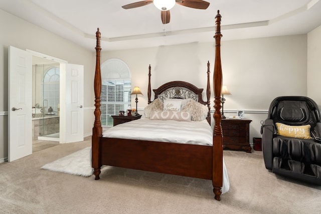 bedroom with light carpet, ensuite bathroom, ceiling fan, and a tray ceiling