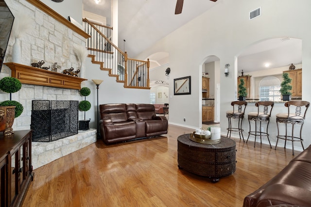 living room featuring light hardwood / wood-style flooring, a fireplace, ceiling fan, and a high ceiling