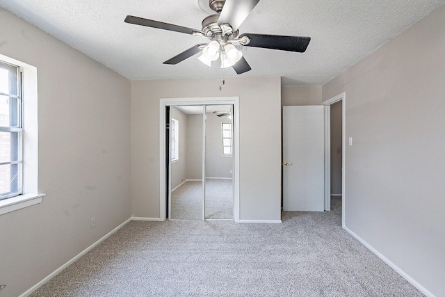 unfurnished bedroom with light carpet, a textured ceiling, a closet, and ceiling fan