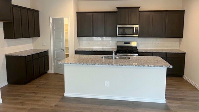 kitchen featuring light stone counters, dark wood-type flooring, stove, a center island with sink, and backsplash