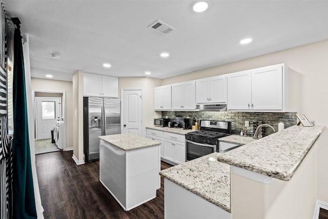 kitchen with a kitchen island, appliances with stainless steel finishes, white cabinetry, kitchen peninsula, and washer and clothes dryer