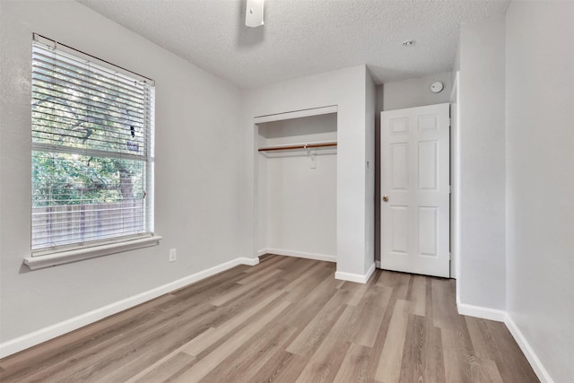 unfurnished bedroom with ceiling fan, a textured ceiling, light wood-type flooring, and a closet