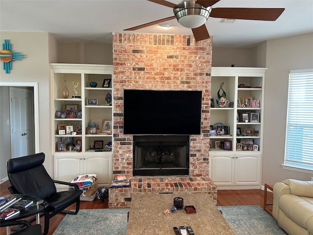 living room with ceiling fan, brick wall, hardwood / wood-style floors, and a brick fireplace