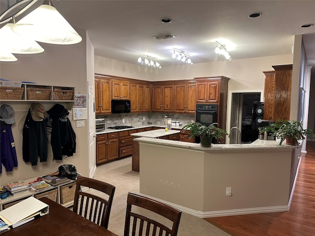 kitchen featuring backsplash, light hardwood / wood-style floors, black appliances, rail lighting, and kitchen peninsula