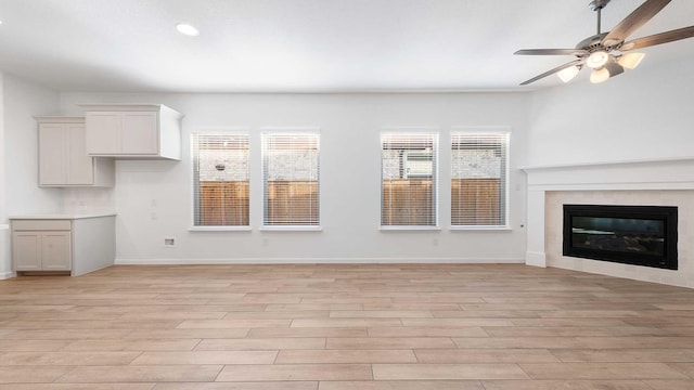 unfurnished living room with a tile fireplace, ceiling fan, and light hardwood / wood-style flooring